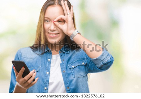 Young beautiful caucasian woman texting sending message using smartphone over isolated background with happy face smiling doing ok sign with hand on eye looking through fingers
