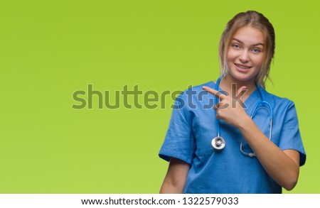 Young caucasian doctor woman wearing surgeon uniform over isolated background cheerful with a smile of face pointing with hand and finger up to the side with happy and natural expression on face