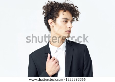 Cute curly guy in a dark suit straightens his jacket on a light background