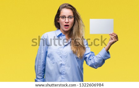 Young beautiful blonde business woman holding blank card over isolated background scared in shock with a surprise face, afraid and excited with fear expression