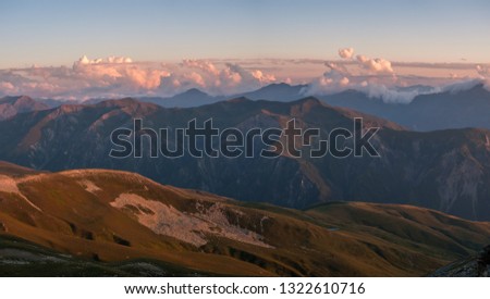 Landscape panorama with mountains ridge and clouds above, evening lights