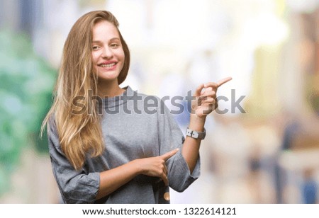 Young beautiful blonde woman over isolated background with a big smile on face, pointing with hand and finger to the side looking at the camera.