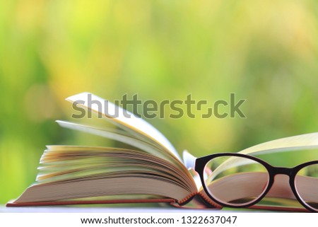 Close-up of open books have glasses placed nearby green light from nature as background selective focus and shallow depth of field
