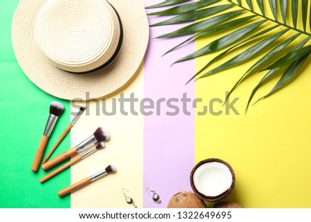 Flat lay composition with beach hat, makeup brushes and tropical leaf on color background