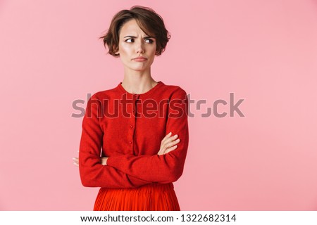 Portrait of an upset beautiful young woman wearing red clothes standing isolated over pink background Royalty-Free Stock Photo #1322682314