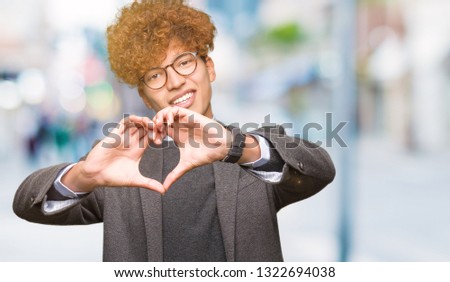 Young handsome business man with afro wearing glasses smiling in love showing heart symbol and shape with hands. Romantic concept.