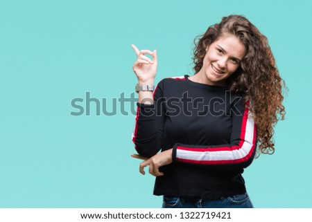 Beautiful young brunette curly hair girl wearing casual look over isolated background with a big smile on face, pointing with hand and finger to the side looking at the camera.