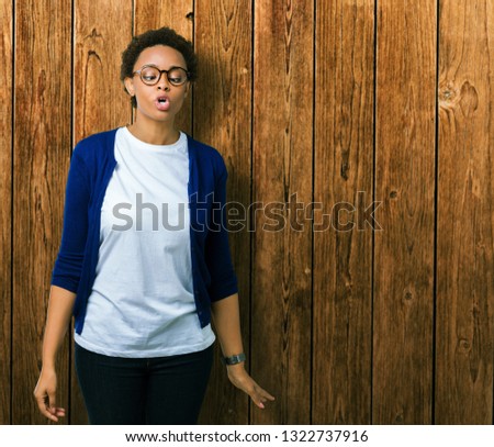 Young beautiful african american woman wearing glasses over isolated background making fish face with lips, crazy and comical gesture. Funny expression.