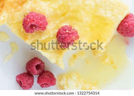 Close-up piece of traditional curd casserole with raspberries and honey on white plate.