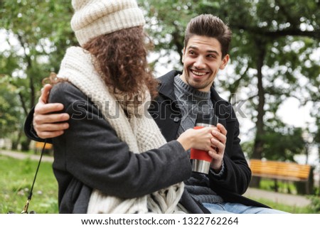 Image of a happy young loving couple drinking tea or coffee outdoors in park talking with each other.