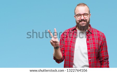 Young caucasian hipster man wearing glasses over isolated background smiling with happy face winking at the camera doing victory sign. Number two.