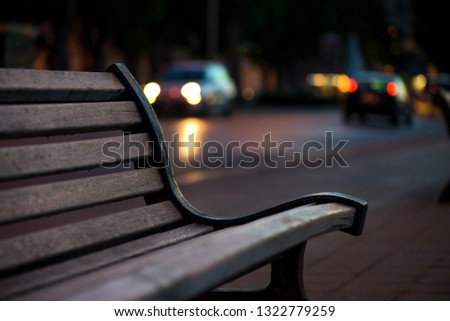 Empty wooden bench in Bari, Italy. Busy street and traffic with cars anr lights in background. Concept of loneliness

