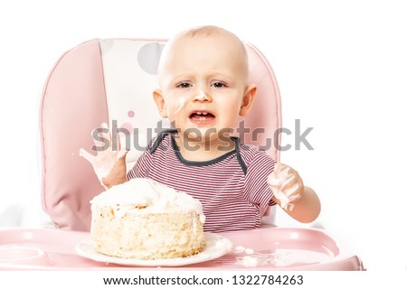 Portrait Of Young Baby Boy eating cake by hands and sitting in high chair. Self feeding concept. Isolated on white background copy space for your text.