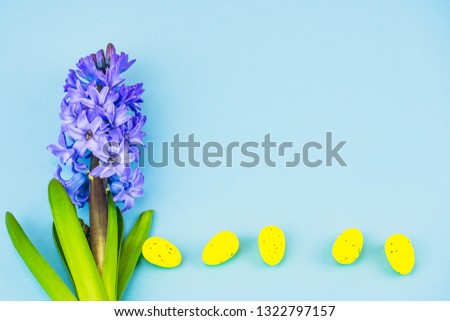 Lilac spring flowers on a blue background. Next to the hyacinth on the bottom edge are yellow eggs in a row. The concept of spring and Easter. There is a place for signature