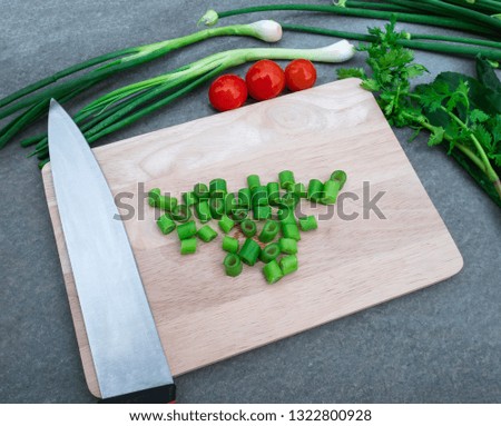 Onion flower cut into small pieces on a wooden cutting board that is placed on a gray floor, green onion , tomato, coriander as a component on table.