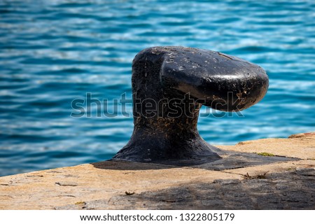 Large black mooring bollard on the quay of the port with sea water in the background