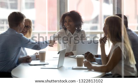African American team leader shaking hand of businessman at company meeting in boardroom, greeting or getting acquainted, colleagues sitting at table together at business briefing or negotiations