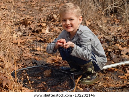 Child catching tadpoles, fish, frogs, crayfish and other aquatic animals in a pond with a net