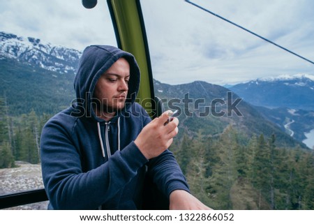 young male taking photos using his mobile phone from cable car cabin in beautiful mountain landscape in Canada