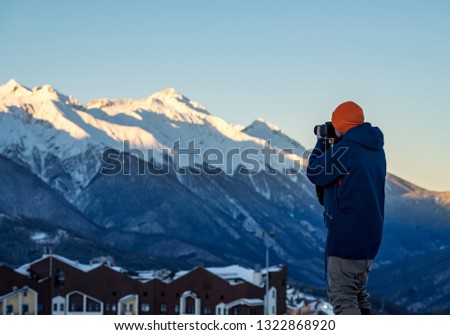Photographer traveler with camera takes pictures of the snowy mountains in early morning at dawn on winter resort of Krasnaya Polyana. Vacations adventure lifestyle