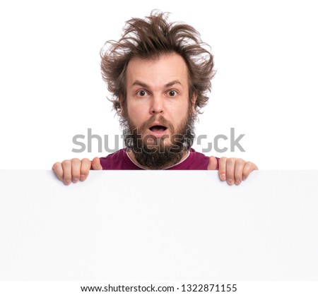 Crazy bearded Man with funny Haircut showing empty blank signboard with copy space. Guy with surprised eyes and mouth open peeking out from behind big white banner, isolated on white background.