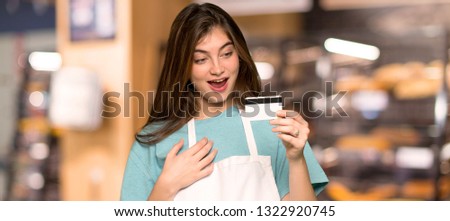 Girl with apron holding a credit card and surprised in a bakery