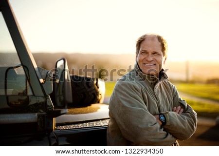 Smiling mid adult man leaning against a vehicle with his arms crossed.