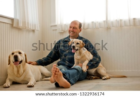 Middle aged man sitting on the floor of his bedroom with his two Labrador dogs.