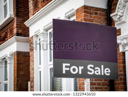 Estate agent 'For Sale' sign board with brick houses in background