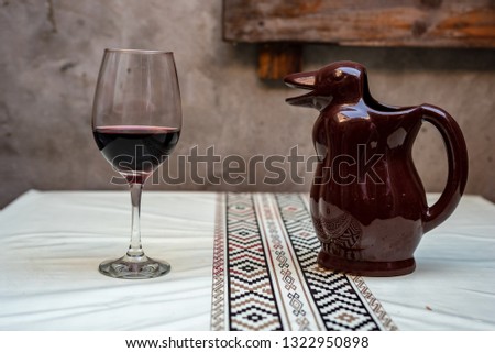 A glass and a wine penguin resting on a white table with a pampa protector on its side and a piece of wooden pallet on the back