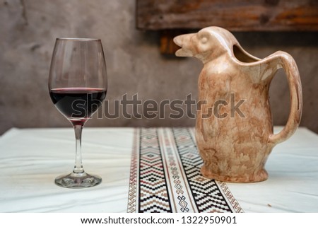 A glass and a wine penguin resting on a white table with a pampa protector on its side and a piece of wooden pallet on the back
