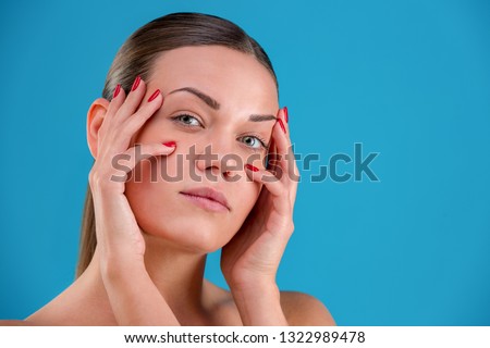 Close up Beauty portrait of young woman brunette smiling and touching her face on blue background. Perfect Fresh Skin. Youth and Skin Care Concept.