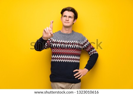 Teenager man over yellow wall with fingers crossing and wishing the best