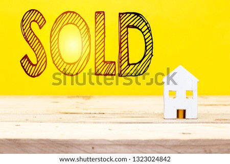sold home, sold text and small white wood house on table with yellow backdrop