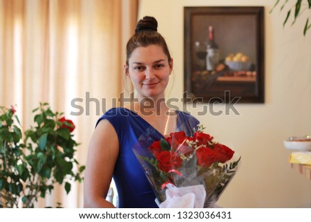 Smiling young woman wearing blue dress holding roses at Mother's Day in soft toned background