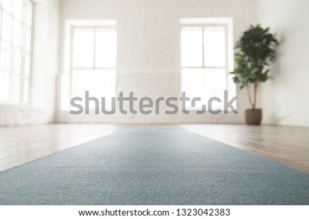 Close up unrolled yoga mat on wooden floor in empty room, modern yoga studio or fitness center with big windows and white brick walls, sport equipment for meditating or exercises Royalty-Free Stock Photo #1323042383
