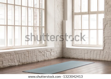 Yoga mat on natural wooden floor in empty room in fitness center, comfortable space for doing sport exercises, big windows and white brick walls, modern yoga class room with nobody Royalty-Free Stock Photo #1323042413