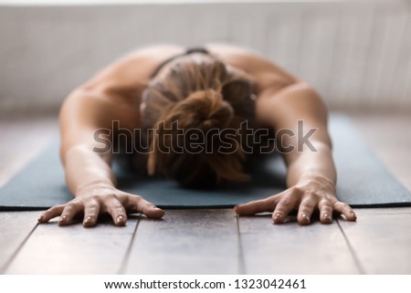 Beautiful girl practicing yoga, relaxing after training on mat, lying face down, attractive young woman working out at home or in modern yoga studio with natural wooden floor close up Royalty-Free Stock Photo #1323042461