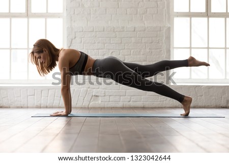 Sporty woman in grey sportswear, bra and leggings practicing yoga, doing Push ups or press ups exercise, phalankasana, variation of Plank pose, beautiful girl working out at home or in yoga studio Royalty-Free Stock Photo #1323042644