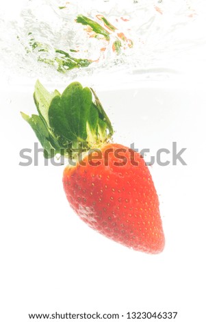 Fresh strawberry dropped into clear water with splash isolated on white background. Vertical photo.