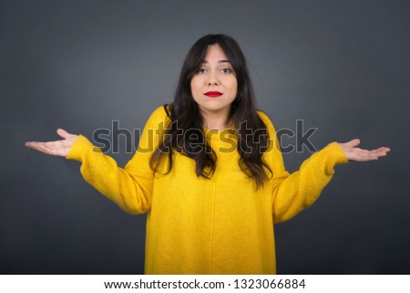 Puzzled and clueless young brunette woman with arms out, shrugging her shoulders, saying: who cares, so what, I don't know. Negative human emotions, facial expressions, life perception and attitude 
