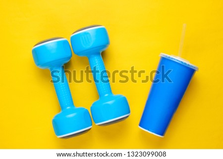 Two blue plastic dumbbells, sport cup on yellow background Sport, fitness concept. Top view. Minimalism