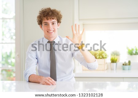 Young business man wearing a tie showing and pointing up with fingers number five while smiling confident and happy.