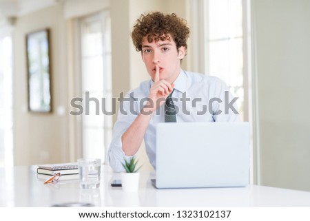 Young business man working with computer laptop at the office asking to be quiet with finger on lips. Silence and secret concept.