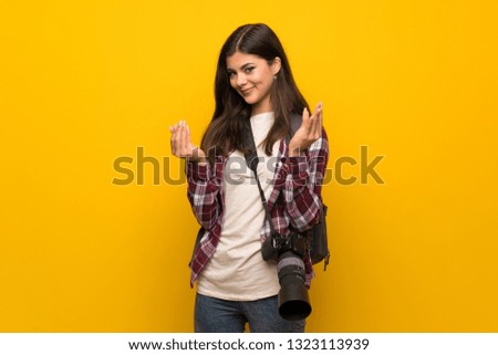 Photographer teenager girl over yellow wall making money gesture