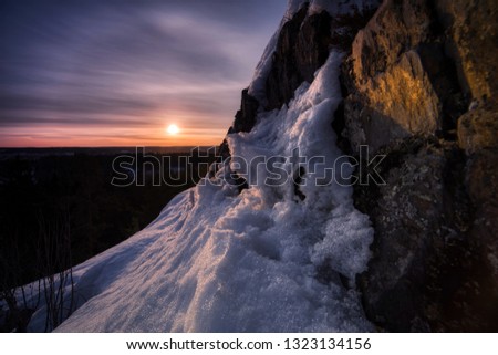 Golden hour sunset view with snow covered rocky cliff in foreground lit by the sun.
