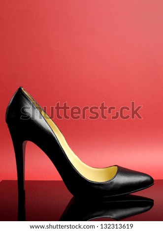 Black stiletto high heel female shoe on red background for iconic symbol of women, femininity, fashion and beauty - vertical with copy space for your text here.