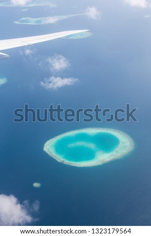 aerial shot from the illuminator of an airplane of the paradise like maldives archipelago with turquoise indian ocean water and beautiful atolls, coral islands, blue lagoons, reefs, white clouds