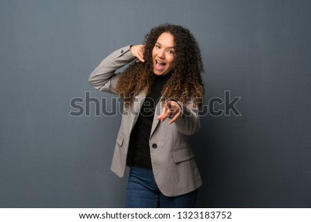 Teenager girl over blue wall making phone gesture and pointing front