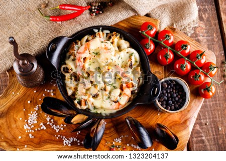 Delicious seafood in white sauce on a metal black plate, a number of products for cooking, tomatoes, champignons. Top view